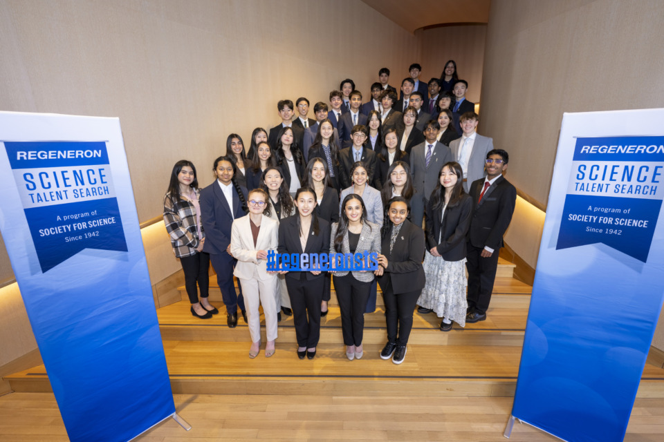 2025 STS Finalists group photo on stairs at the Conrad Hotel. Two blue Regeneron STS banners are placed on the sides of the group shot.