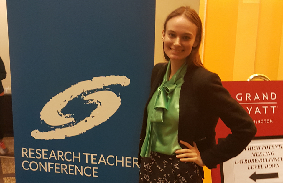 A woman posing in front of a blue Society for Science sign is wearing a green shirt with a black blazer.